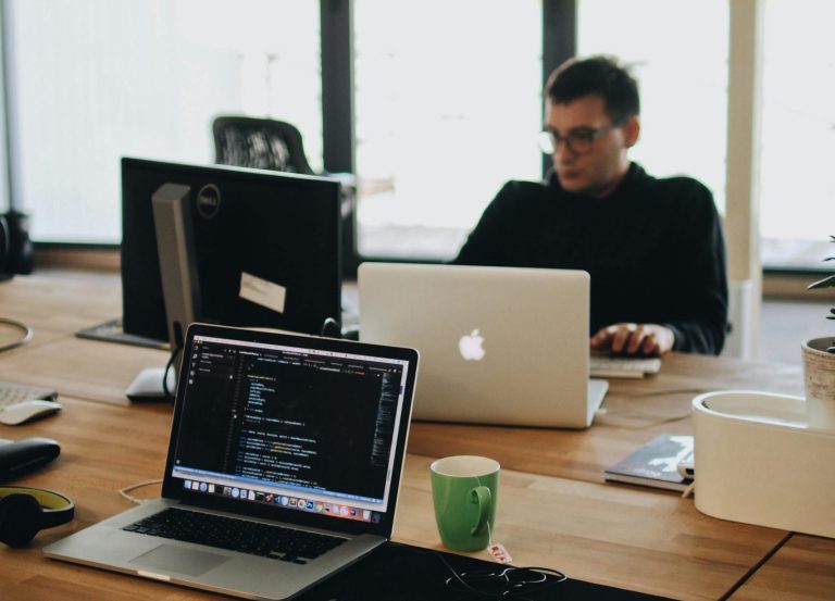 A web developer working on code in a modern office setting with multiple devices.